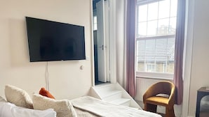 A bedroom with a bed, a chair, a television, and a window with curtains.