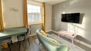 A room with a dining table, two chairs, a sofa, a TV, and a small table with a remote. - Playful 1 bed in Camden (Greater London)