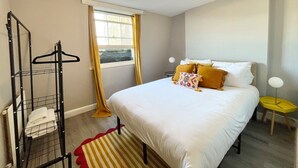 A neatly arranged bedroom with a bed, a hanging clothes rack, a small table, and a window with curtains. - Playful 1 bed in Camden (Greater London)