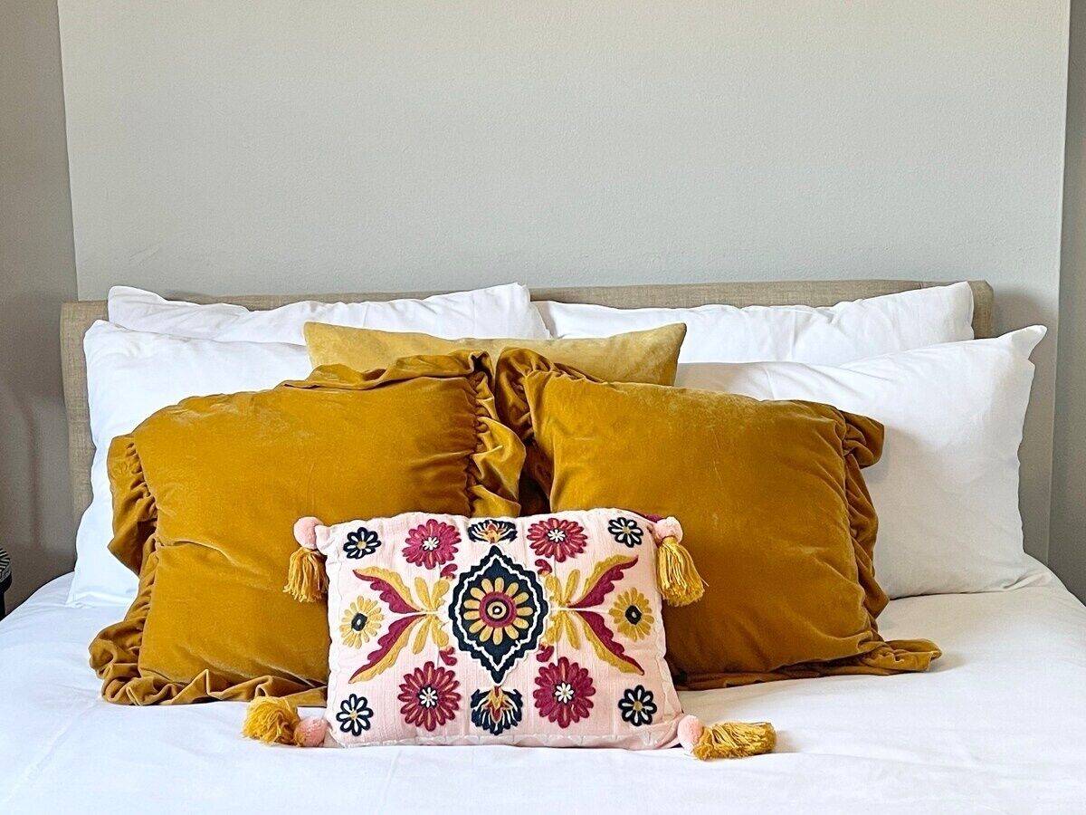 Ein Bett mit weißen und senffarbenen Kissen, eines davon mit einem Blumenmuster.
