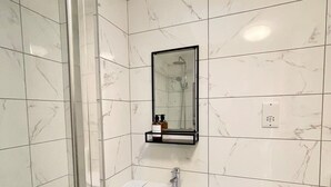 A modern bathroom with white marble tiles, a glass shower enclosure, a white sink, and a mirror above the sink. - Playful 1 bed in Camden (Greater London)