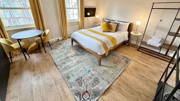 A hotel room with a bed, a small table, chairs, a TV, and a window with curtains. - Cozy studio Flat in Camden (Greater London)