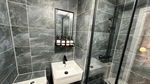 A bathroom with a white sink, a mirror, and a shower area with a glass door. - Cozy studio Flat in Camden (Greater London)