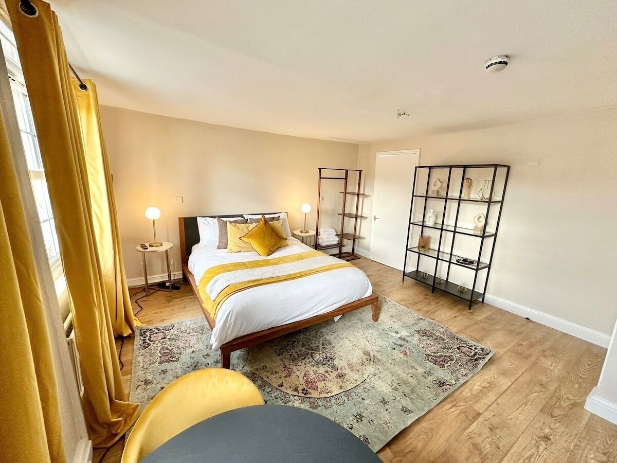 A bedroom with a bed, bedside tables, a nightstand, a mirror, a wardrobe, and a shelf with decorative items.