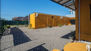 A building with a gravel driveway, a covered outdoor area, and a yellow building with a metal roof. - Container 3 (Navegantes)