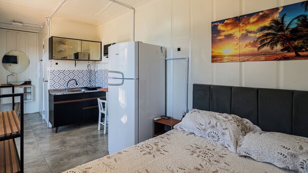 A compact hotel room with a bed, a desk with a chair, a small kitchenette, and a bathroom. - Container 3 (Navegantes)