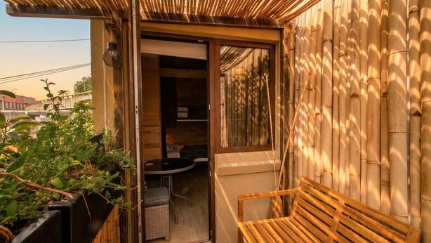 A wooden bench, a small table, and a doorway leading to a room with a window. - LA SELVA HOSTEL (Mexico City)