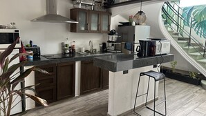 A modern kitchen with dark wooden cabinets, a granite countertop, a stainless steel range hood, and a built-in island with bar stools. - LA SELVA HOSTEL (Mexico City)