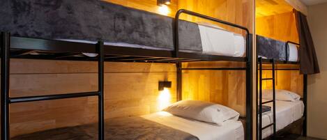 A bunk bed room with wooden walls and a single bedside lamp.