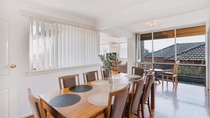 A dining area with a wooden table and chairs, a vase with a plant, and large windows with blinds. - Restful Canberra Retreat in Spacious Terrace Home (Canberra)