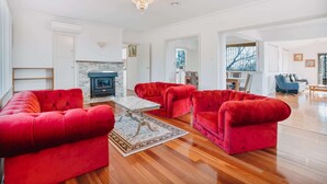 A spacious living room with red sofas, a fireplace, and a chandelier. - Restful Canberra Retreat in Spacious Terrace Home (Canberra)