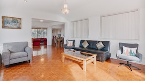 A spacious living room with a wooden floor, a grey sofa, a red couch, and a glass coffee table. - Restful Canberra Retreat in Spacious Terrace Home (Canberra)