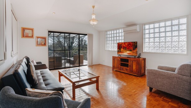 A spacious living room with a large TV, wooden flooring, and a balcony with glass doors. - Restful Canberra Retreat in Spacious Terrace Home (Canberra)