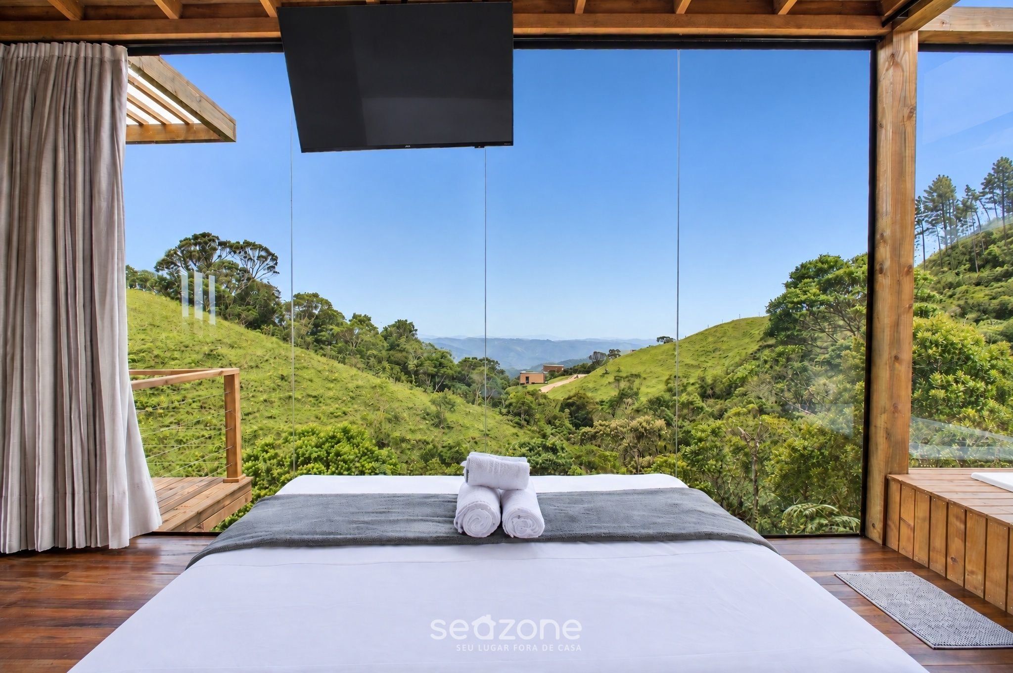 A bedroom with a large bed, a TV, and a view of a green landscape.