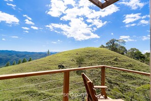 A wooden balcony railing overlooking a grassy hill with a clear sky. - Cabana c\ Jacuzzi prox. de Florianópolis VST026 (Anitapolis)