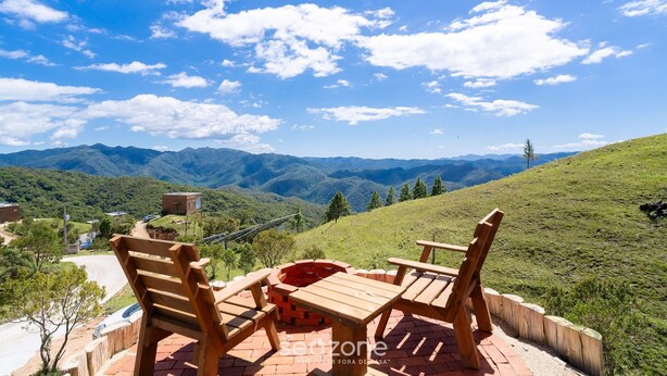 A patio with wooden furniture and a brick fire pit overlooking a mountainous landscape. - Cabana c\ Jacuzzi prox. de Florianópolis VST026 (Anitapolis)