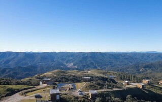 A mountainous landscape with several buildings, including a large structure with a flat roof and smaller buildings with sloped roofs.