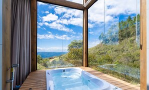 A hot tub on a wooden deck with a scenic view of a forested hillside and mountains.