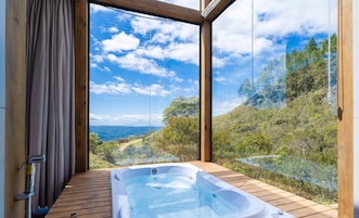 Un jacuzzi en una terraza de madera con una vista panorámica de una ladera boscosa y montañas.
