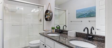 Une salle de bain moderne dotée d’une douche à parois de verre, d’un meuble-lavabo à deux vasques et d’un grand miroir.