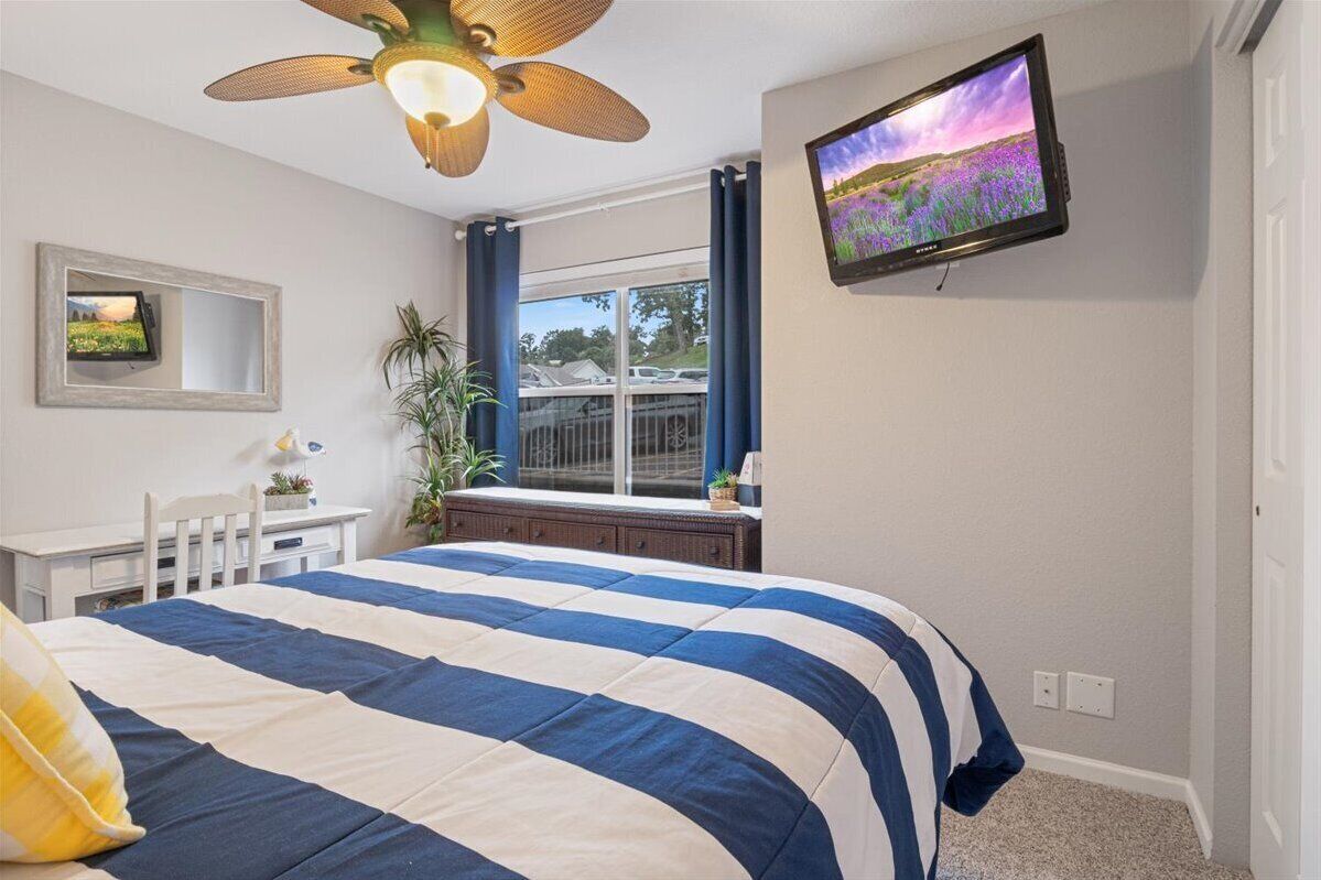 A bedroom with a bed, a desk, a chair, a television, and a window with curtains.