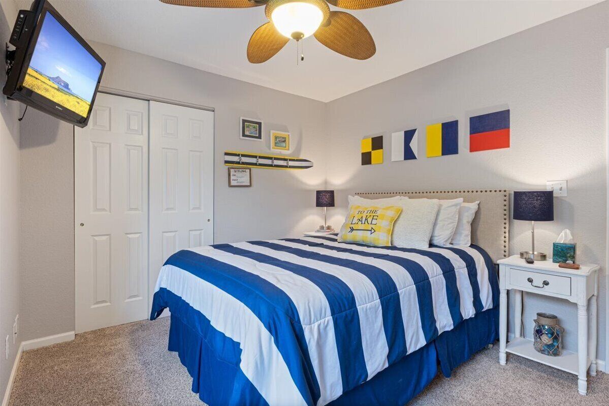 A bedroom with a bed, a nightstand, a television mounted on the wall, and a ceiling fan.