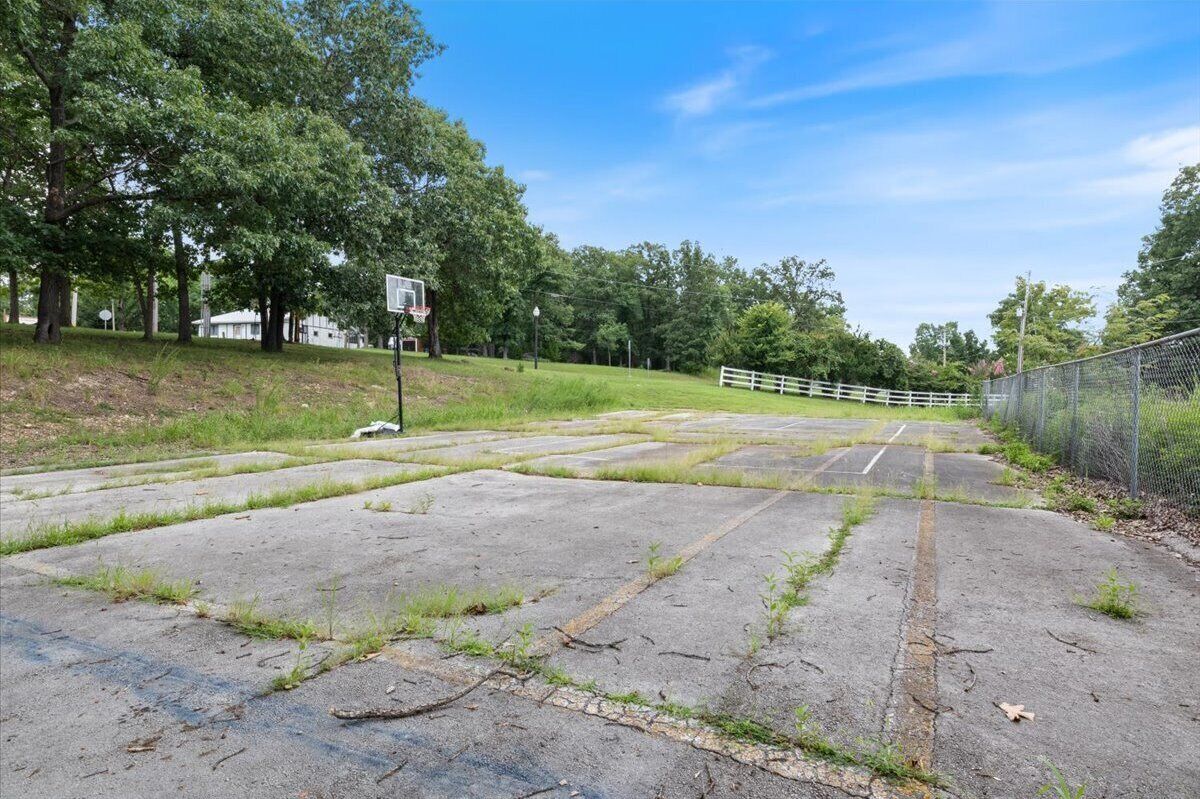 Un terrain de basket-ball avec un panier, entouré d’une clôture et d’arbres.