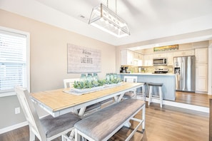 A modern kitchen with white cabinets, a stainless steel refrigerator, and a wooden dining table with benches.