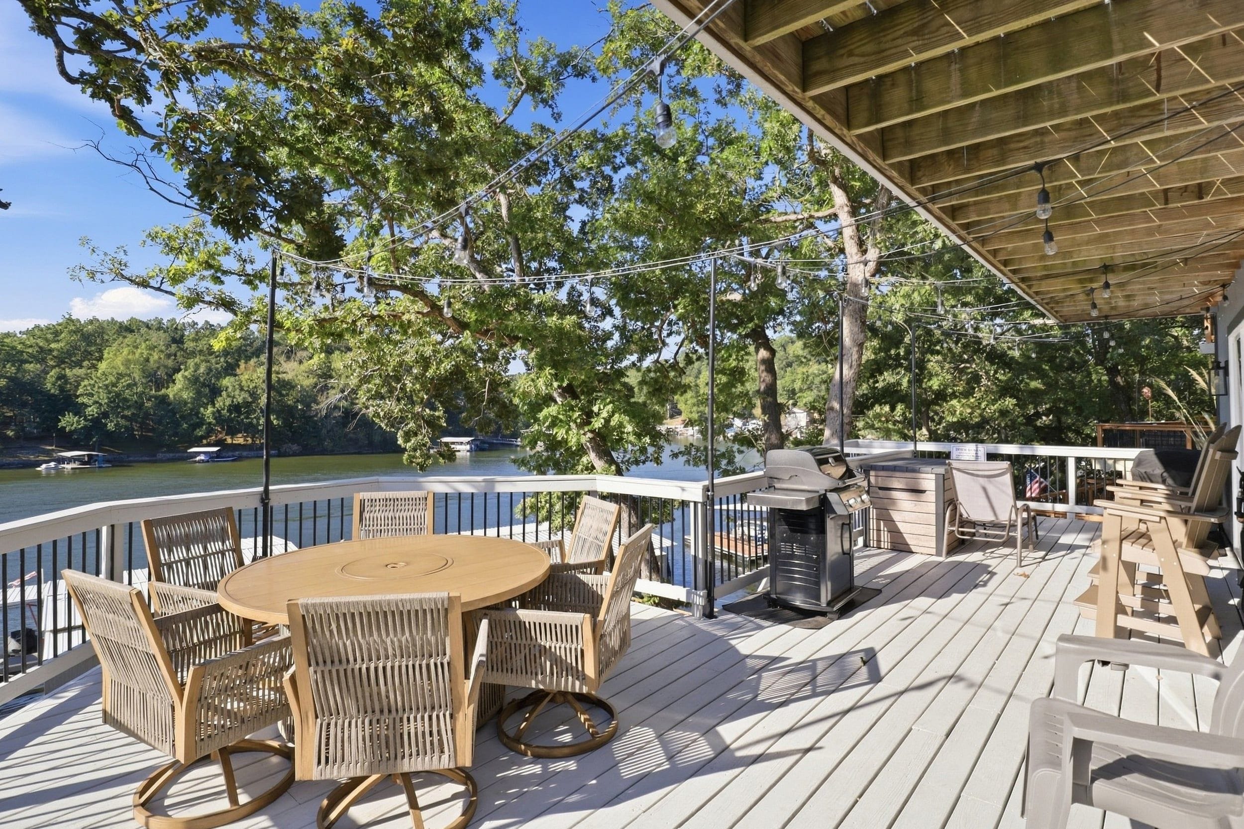 Een terras met een ronde tafel en stoelen, een barbecue en uitzicht op een meer.