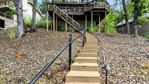A staircase leading to a wooden deck with a railing, surrounded by trees and gravel.