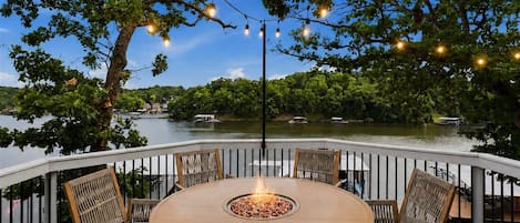 Un área de comedor al aire libre con una mesa redonda y sillas, un hogar de fuego y luces colgantes.