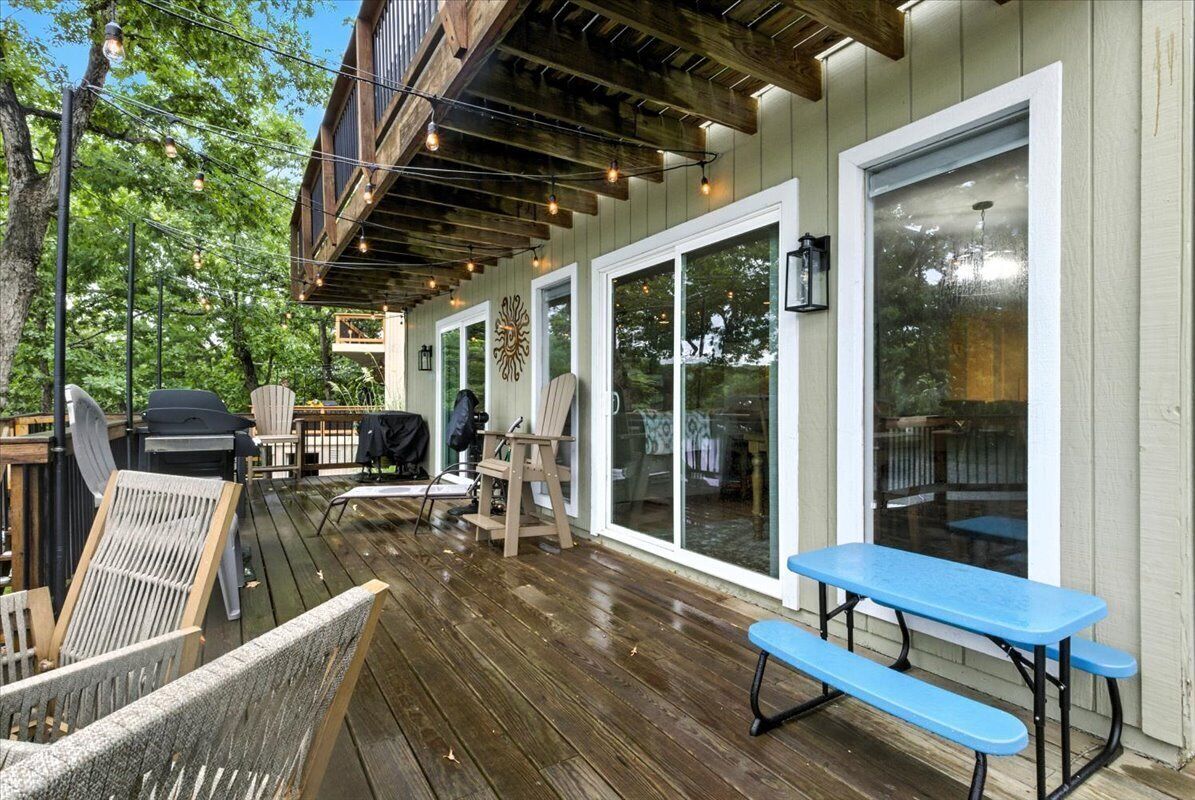 Terraza exterior con piso de madera, una mesa de picnic azul y una parrilla.