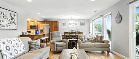 A spacious living room with a ceiling fan, a dining area with a chandelier, and a kitchen in the background.