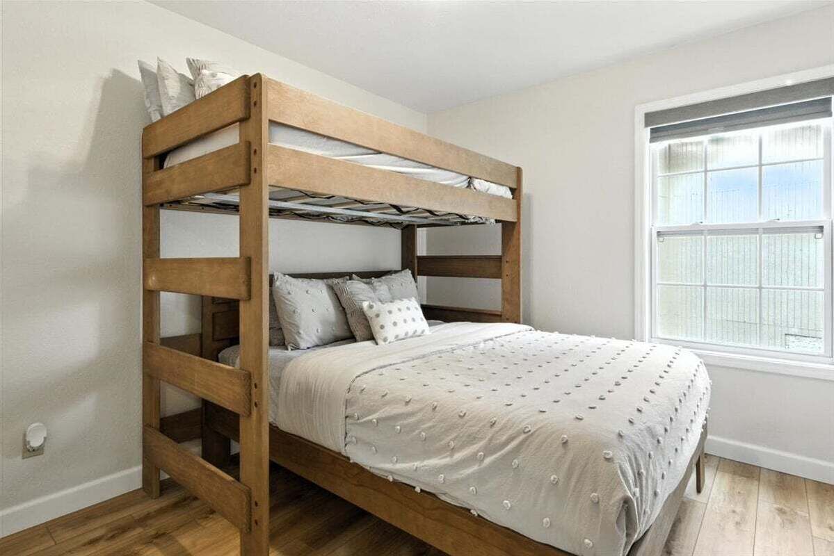 A bunk bed with a wooden frame, white bedding, and a window with blinds.
