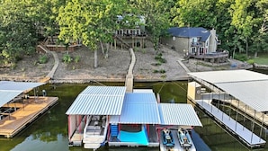 A lakeside property with docked boats, a wooden deck, and a house surrounded by trees.