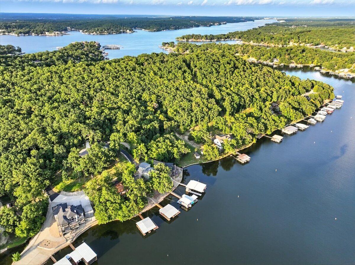 Ovenudblik over en ejendom ved søen med både i havnen, frodig vegetation og en mindre bygning.