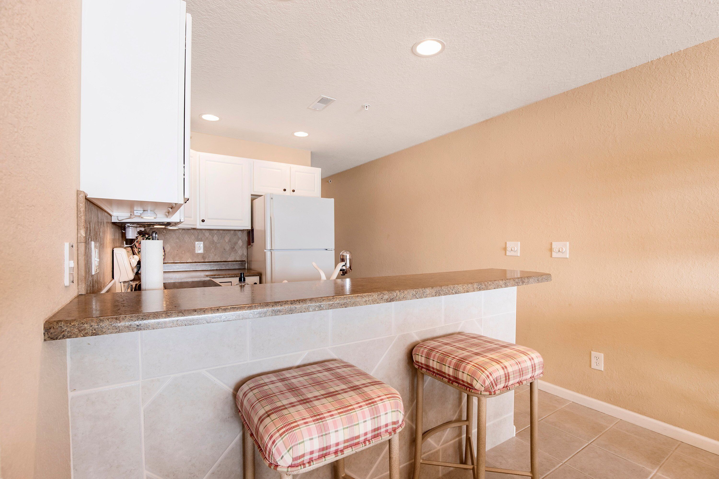 A kitchen with a countertop, two stools, cabinets, and a refrigerator.