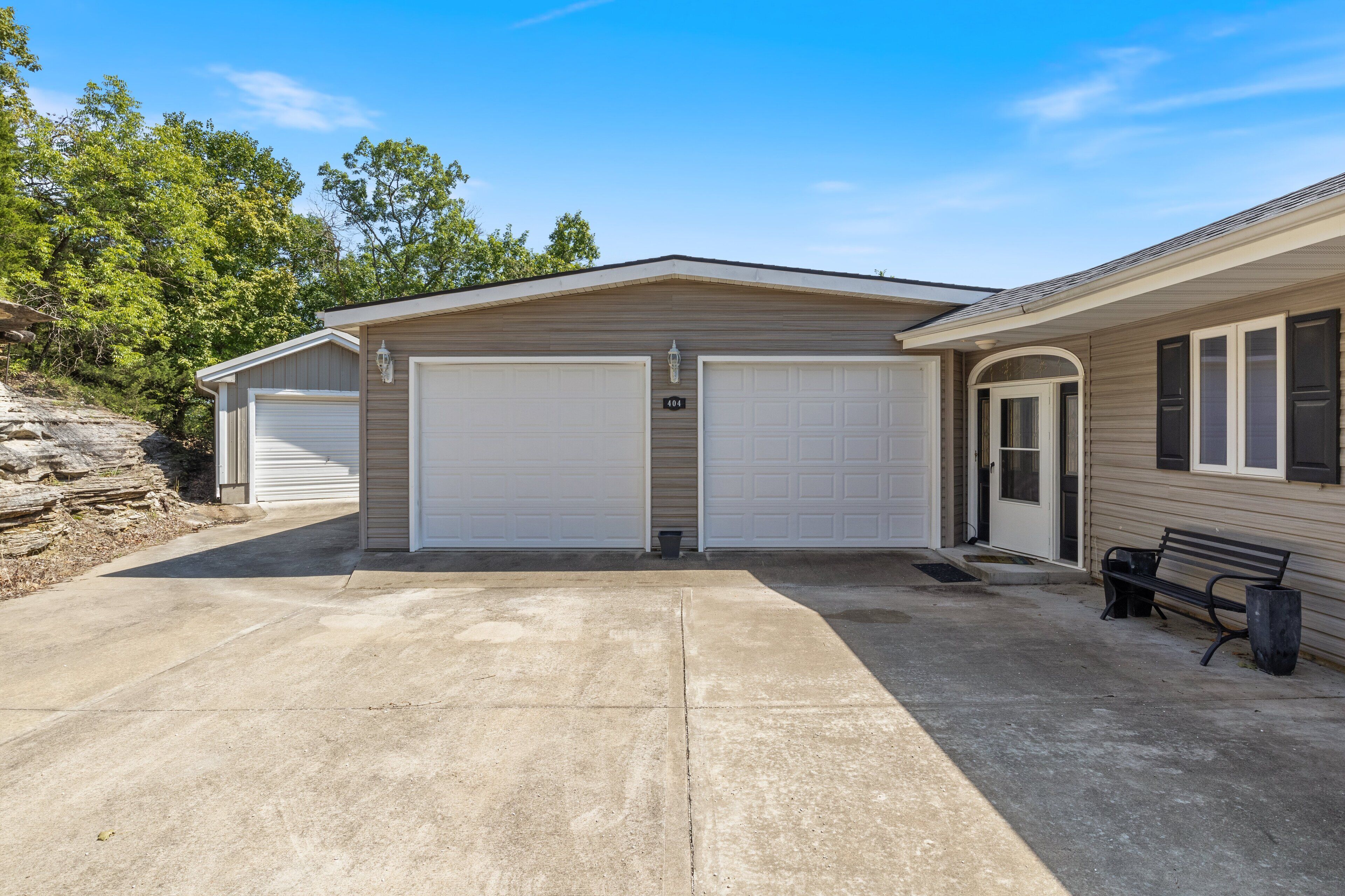 A two-car garage attached to a single-story house with a front door and a bench outside.