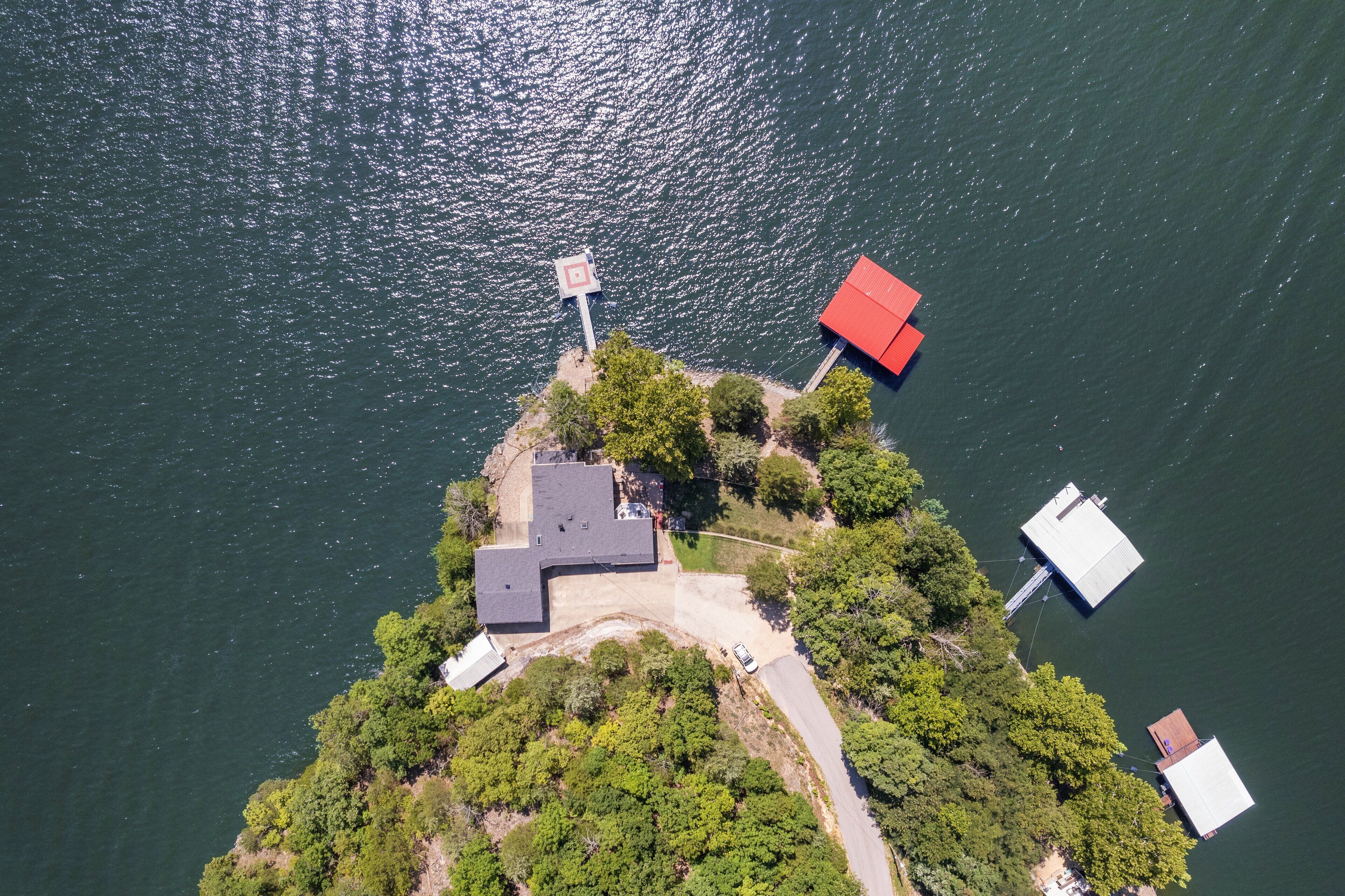 Vista aérea de una propiedad junto al lago con un muelle, un edificio de techo rojo y una estructura de techo blanco.