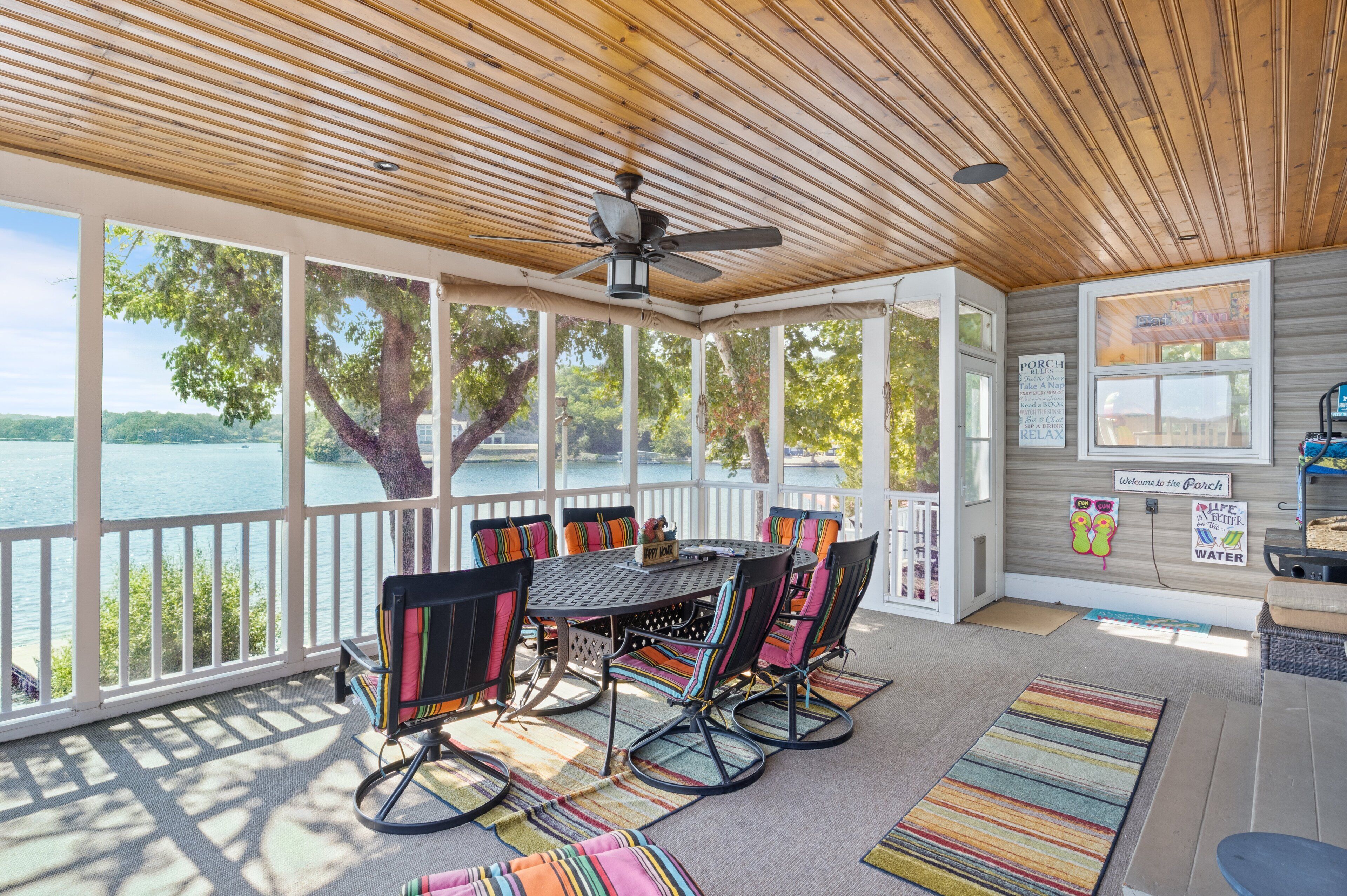 A covered outdoor area with a table and chairs, large windows, and a view of a lake.