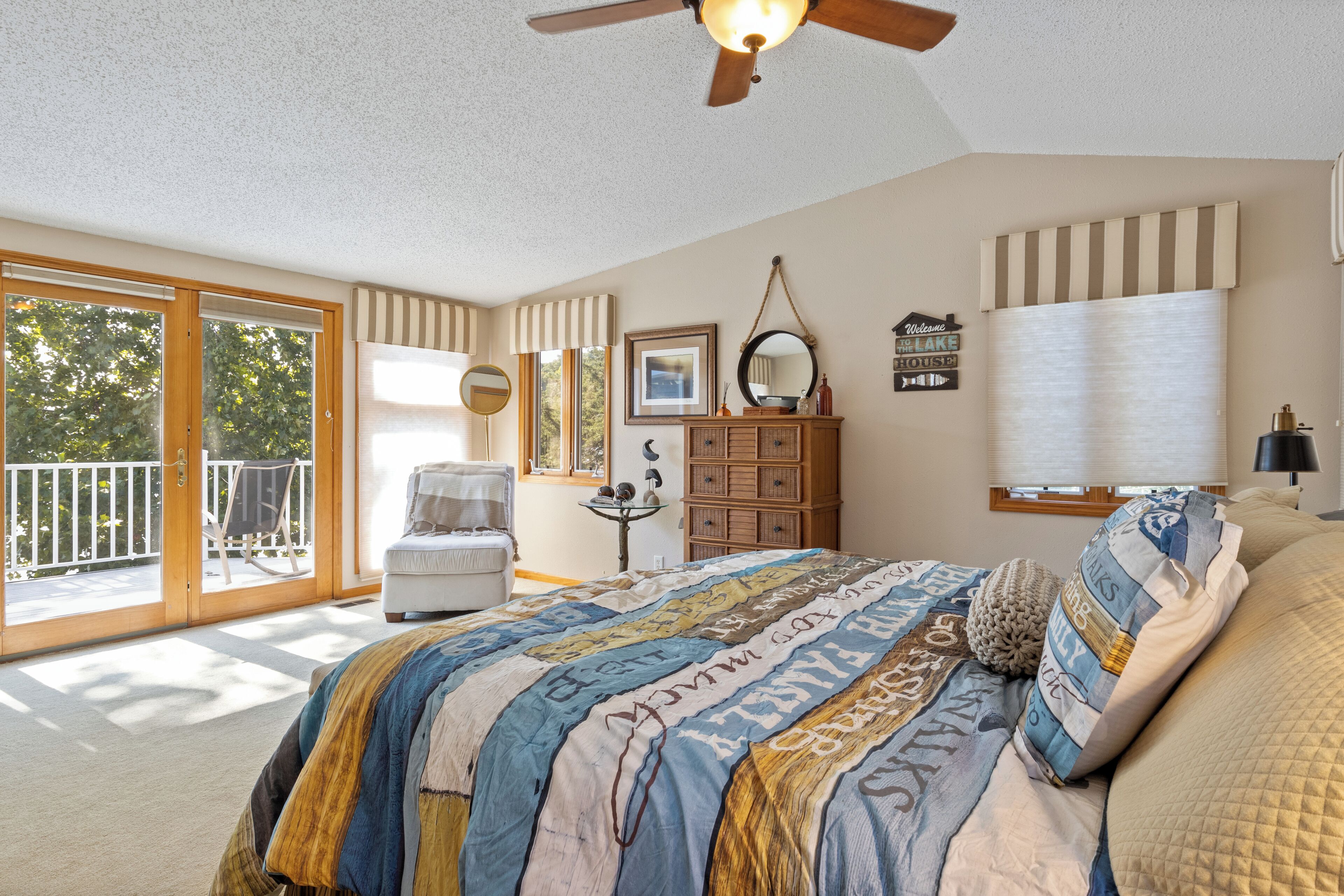 A bedroom with a large bed, a dresser, a chair, and a balcony with a view of trees.