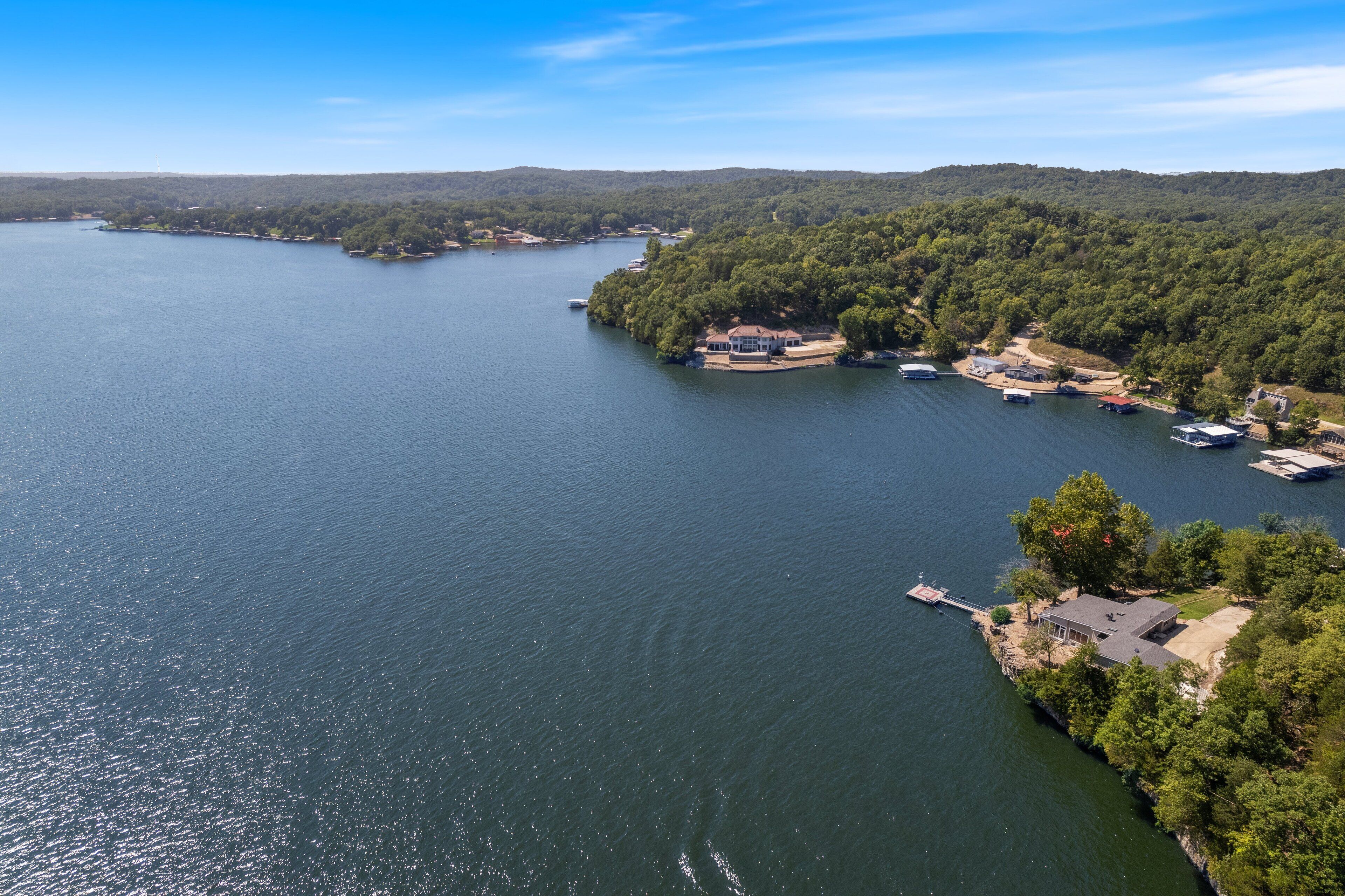 Vista aérea de uma propriedade à beira de um lago, com um píer, barcos e uma casa rodeada por uma floresta densa.