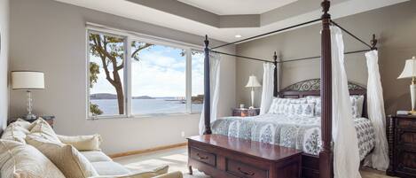 Un dormitorio con cama con dosel, una mesita de noche, un aparador y vistas al exterior.