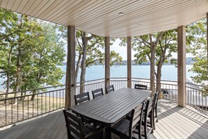 Une terrasse extérieure couverte, dotée d’une table et de chaises, qui offre une vue sur un lac bordé d’arbres et sur une rive éloignée.