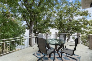 Une terrasse extérieure avec une table et des chaises en verre, une balustrade en pierre et une vue sur une étendue d’eau.
