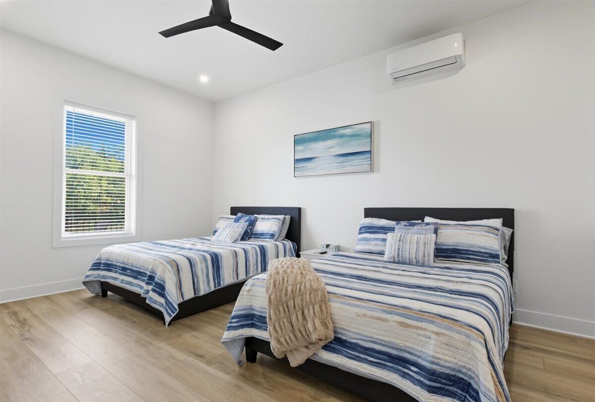 Un dormitorio con dos camas, ventilador de techo, aire acondicionado y ventana con persianas.