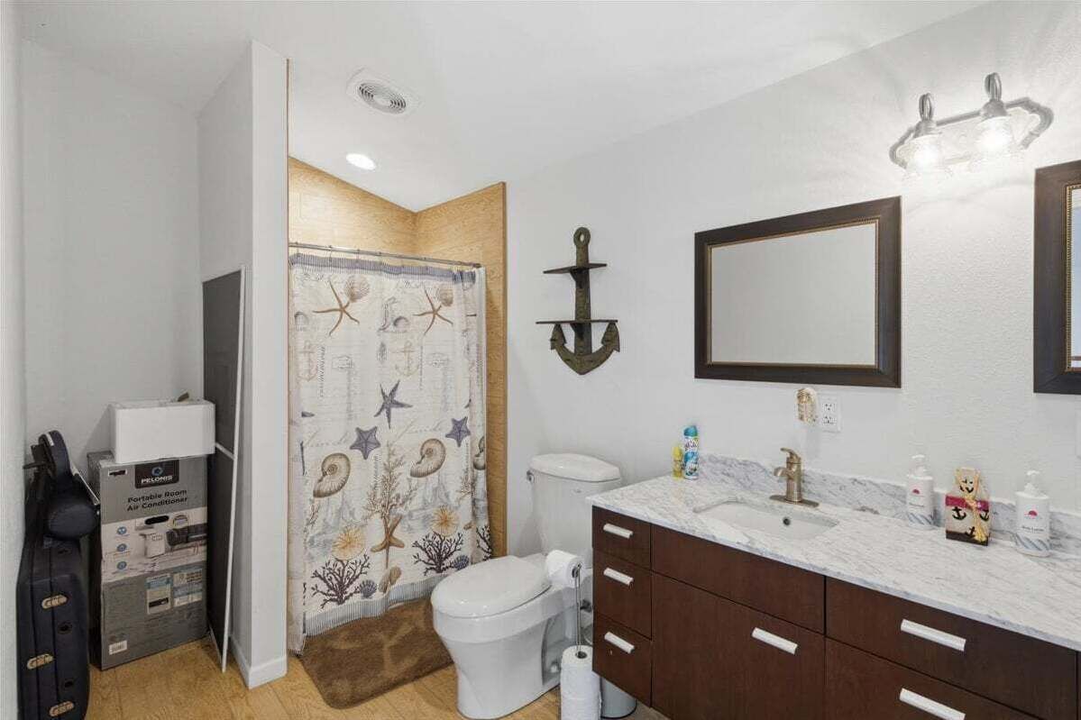 Une salle de bain comprenant des toilettes, un lavabo avec un plan de travail en marbre, un miroir et un rideau de douche à motifs nautiques.