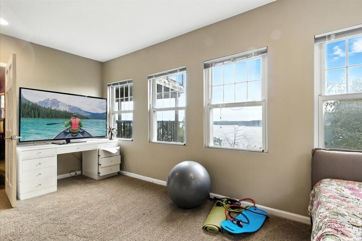 Una camera da letto con una grande TV, una palla da ginnastica, un tappetino yoga e finestre con vista su un lago.