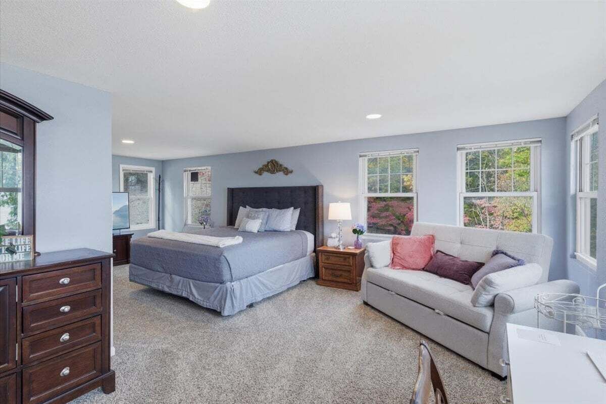 A bedroom with a bed, a dresser, a nightstand, a lamp, and a sofa.