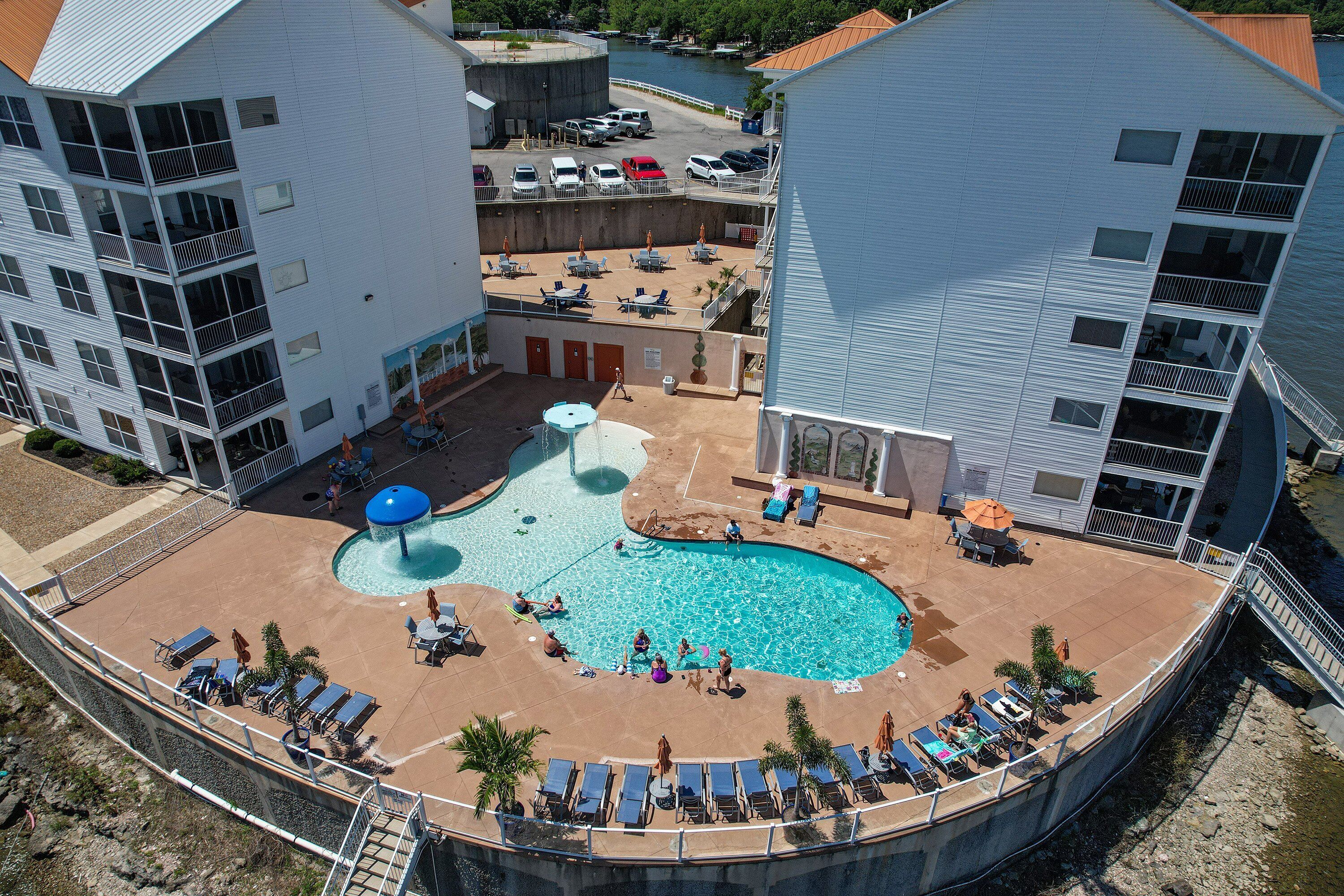 Un espace piscine agrémenté de chaises longues et de parasols, entouré de bâtiments dotés de balcons et offrant une vue sur l’eau.